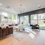 A stylish, modern living room with lots of seating, large windows, and sliding glass doors leading to the backyard